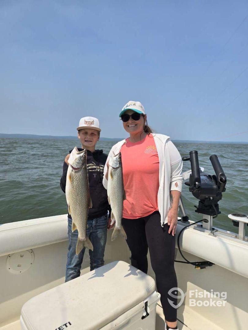 A young angler and an adult proudly displaying their catch of two large Lake Trout while enjoying a day on the water.