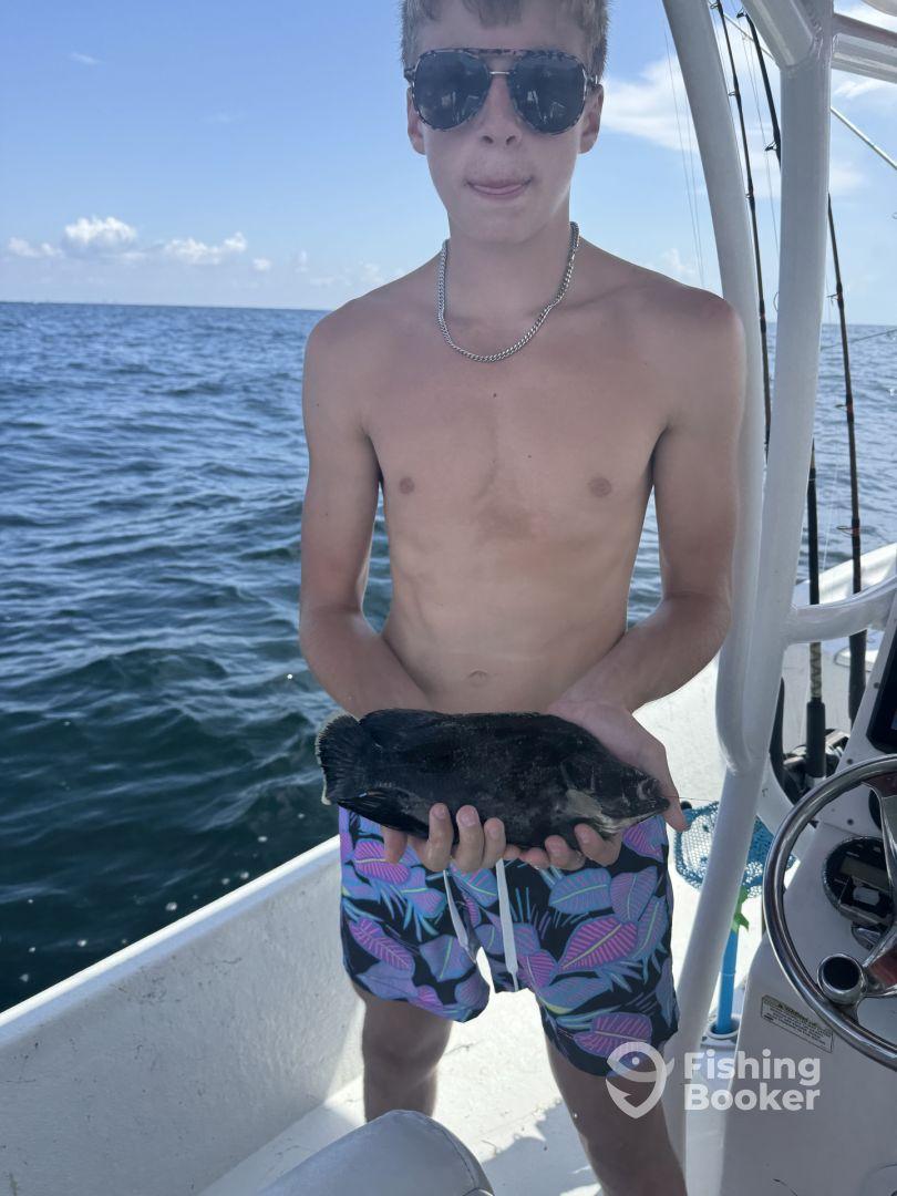 A young angler proudly displaying a black fish while aboard a fishing boat, enjoying a sunny day on the water.