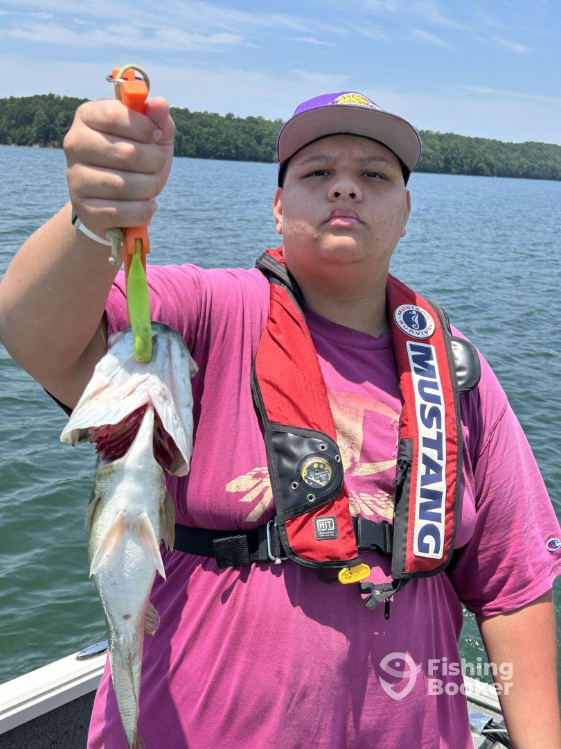 Young angler proudly displaying a freshly caught fish while on a boat, surrounded by a scenic lake backdrop.