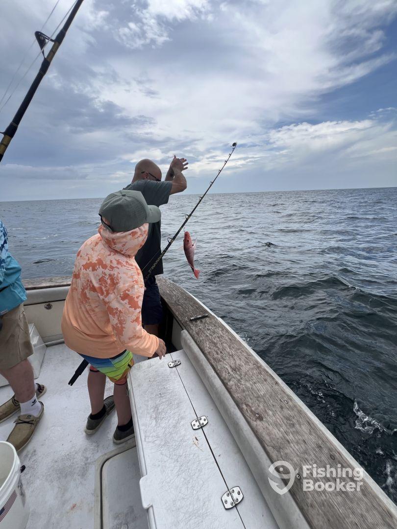 A young angler and an adult are actively fishing on a boat, with a Red Snapper being reeled in during a Gulf fishing trip.