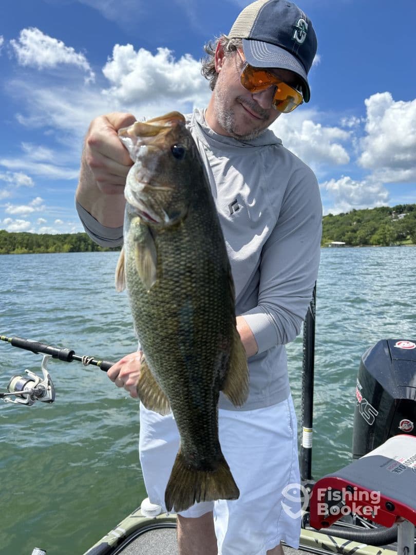 An angler proudly displaying a large Largemouth Bass while fishing on a sunny day, showcasing the beautiful lake environment.