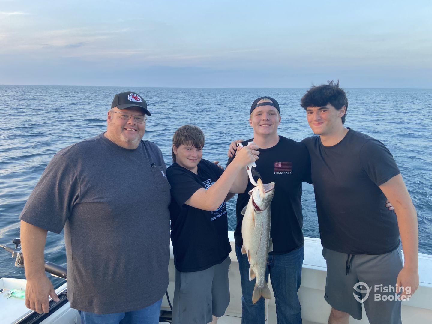 A family of four proudly displaying a large caught fish while enjoying a fishing trip on the open water.