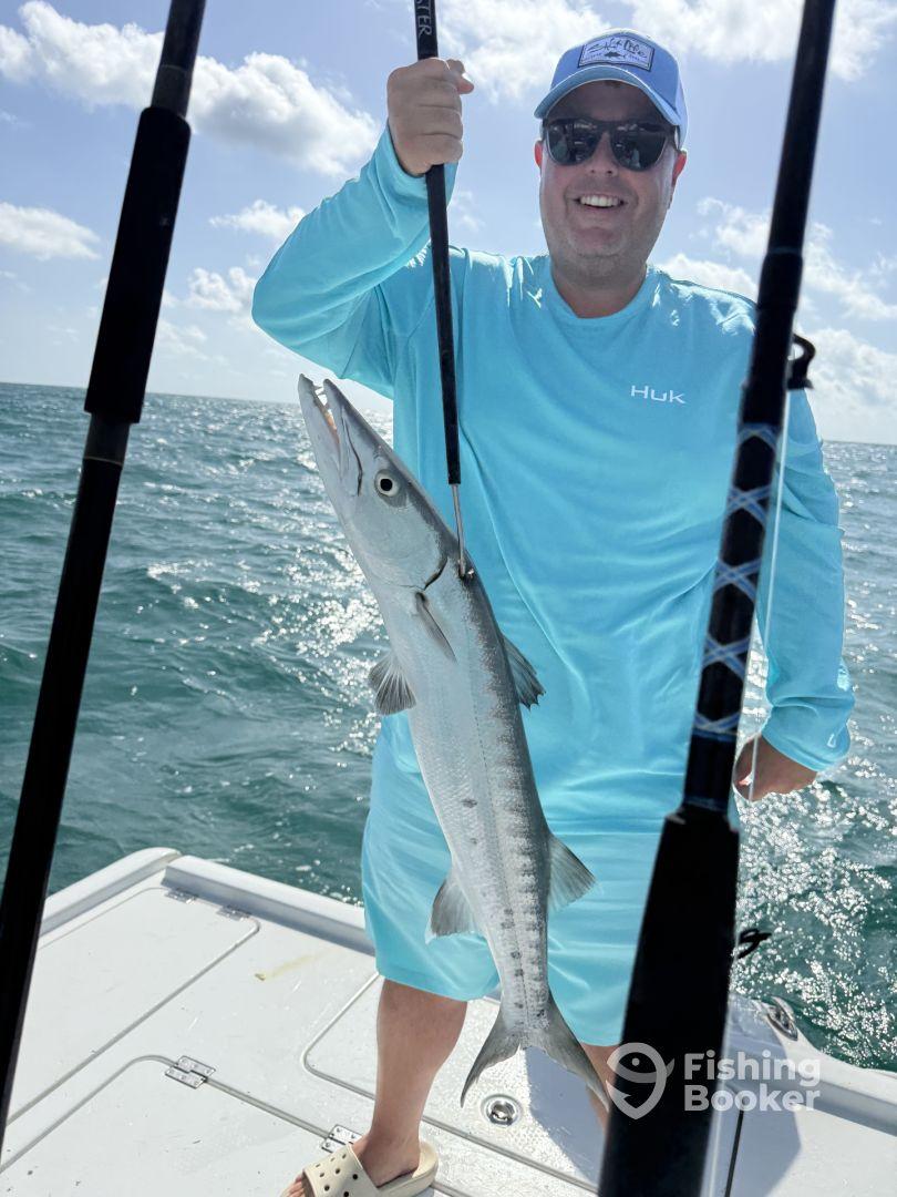 Angler proudly displaying a Barracuda while fishing on a sunny day in open waters.