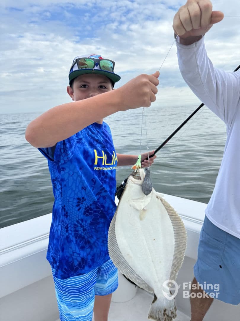 A young angler proudly displaying a large Flounder while fishing on a boat, showcasing the excitement of a successful catch.