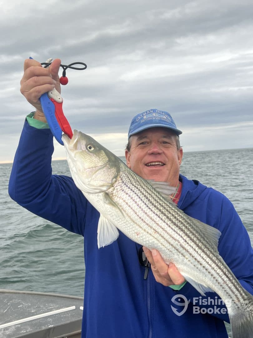 An angler proudly displaying a large Striped Bass while fishing on a boat, showcasing a successful day on the water.