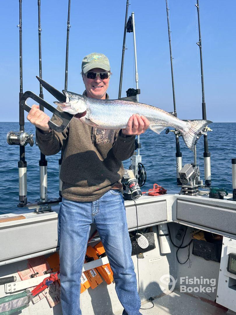 An angler proudly displaying a large Salmon aboard a fishing boat, showcasing a successful day on the water.