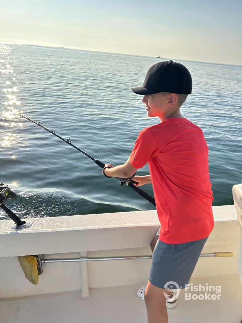 A young angler casting a line while fishing on a boat in calm waters, showcasing the excitement of a fishing adventure.