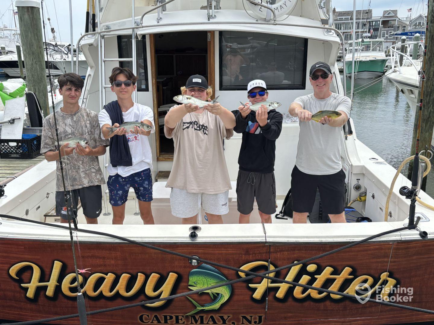 A group of young anglers proudly displaying their catch of striped bass in front of the 'Heavy Hitter' charter boat in Cape May, NJ.