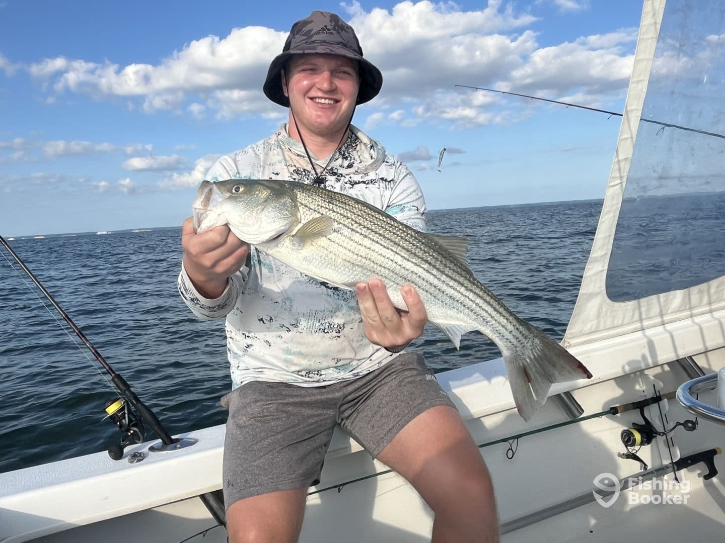 Angler proudly displaying a large Striped Bass while fishing on a boat in open waters.