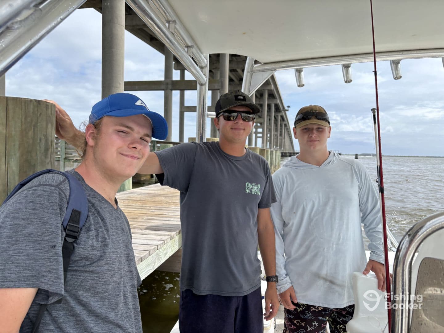 Three young anglers posing on the boat, ready for a fishing adventure, with a scenic view of the water and dock in the background.