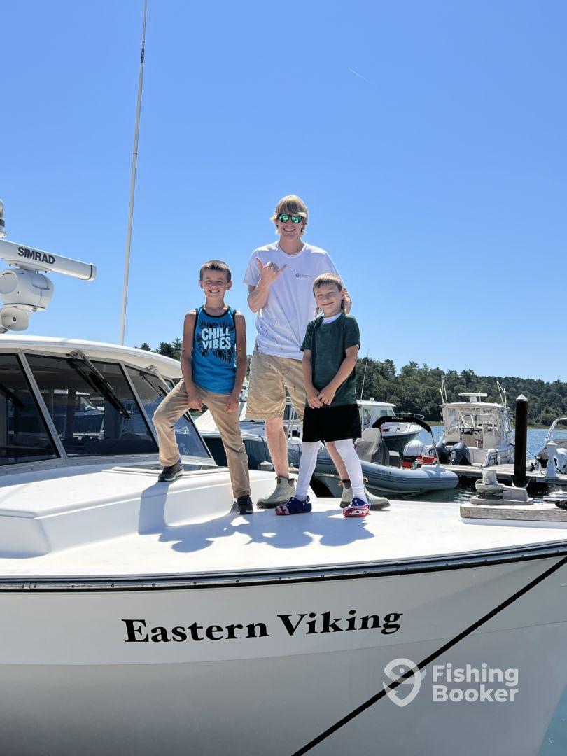 Three young anglers posing on the bow of the Eastern Viking, showcasing a fun day at the marina.