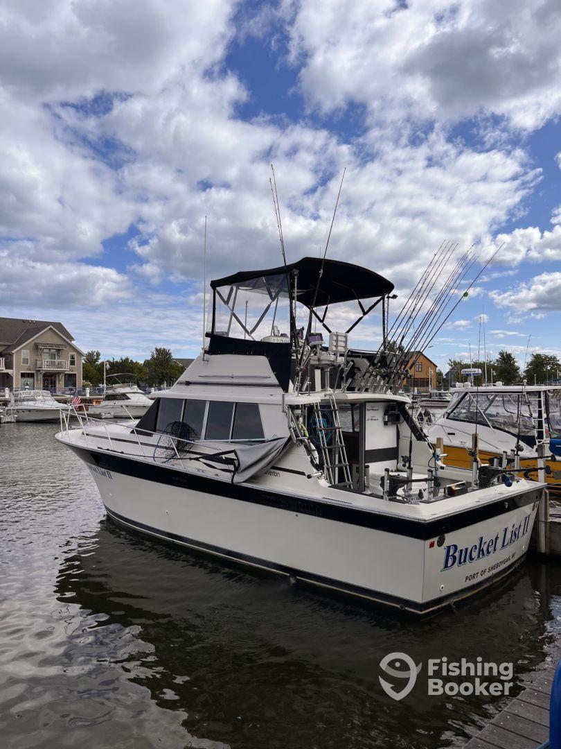 The 'Bucket List II' fishing charter boat docked at a marina, showcasing its spacious design and fishing gear setup under a cloudy sky.