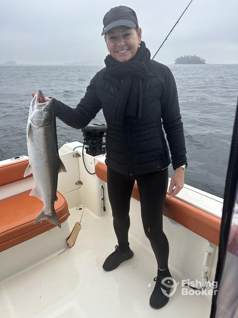 An adult angler proudly displaying a large Silver Salmon aboard a fishing boat in overcast weather.