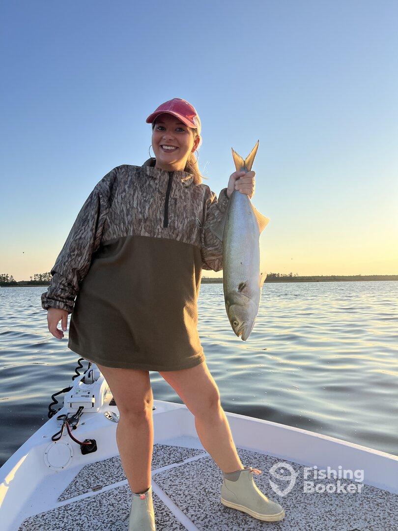 Angler proudly displaying a large fish while standing on the bow of a boat during a sunset fishing trip.