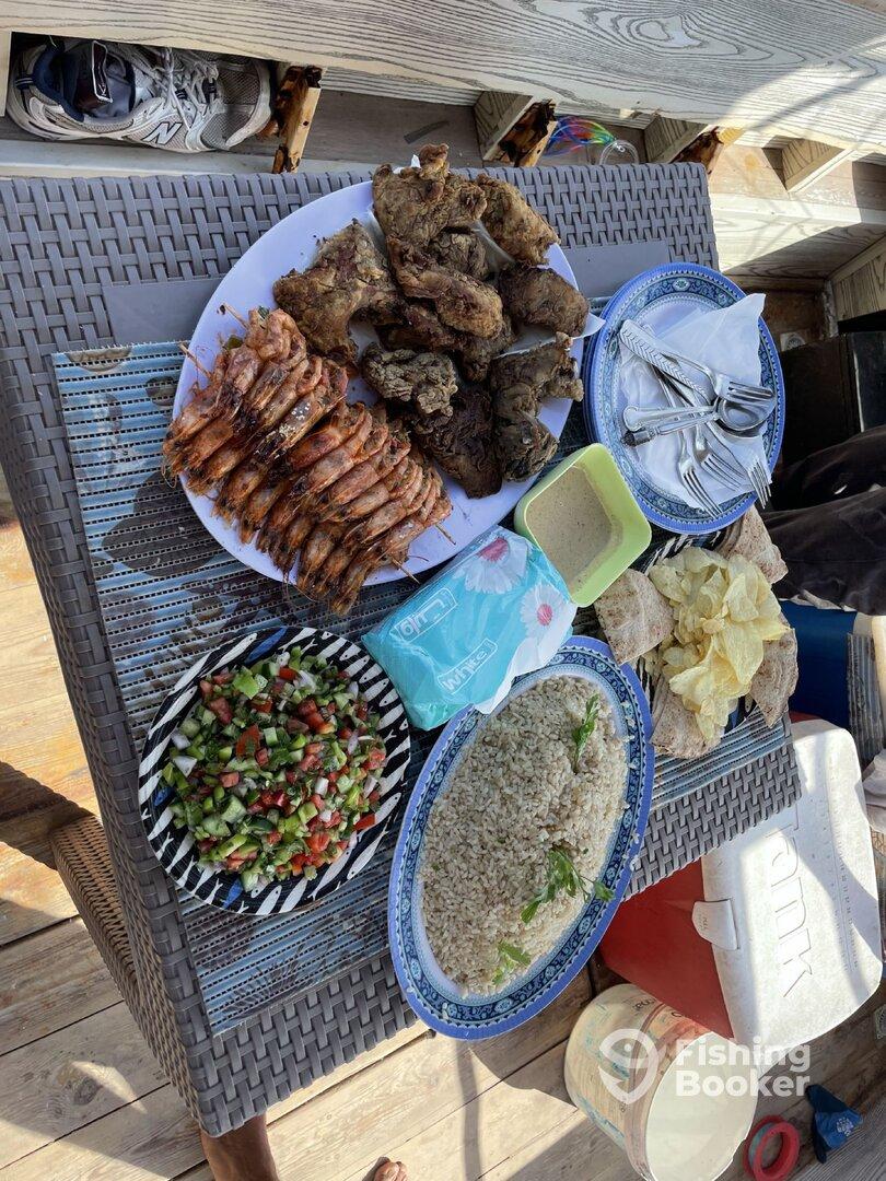 A spread of grilled food including shrimp and chicken, displayed on a table, likely after a fishing trip.