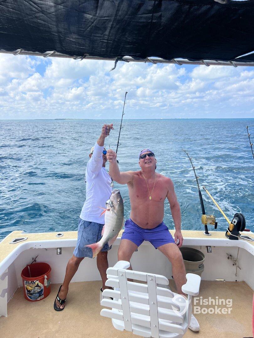 Two anglers celebrating a successful catch of a Snapper while fishing on a charter boat in open waters.