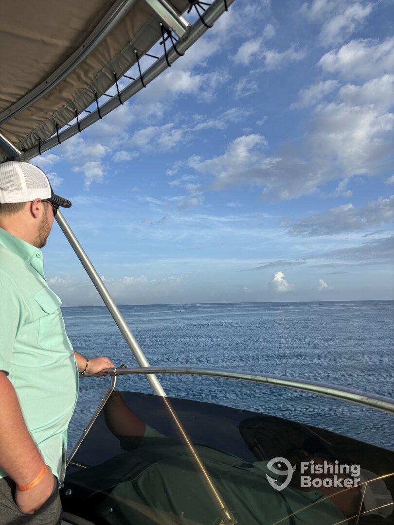 A man enjoying the serene view from the helm of a boat, surrounded by clear skies and calm waters.