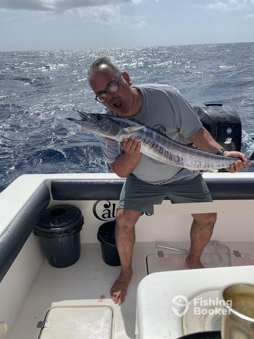 An excited angler proudly displaying a large Wahoo while fishing offshore, showcasing the thrill of deep-sea fishing.