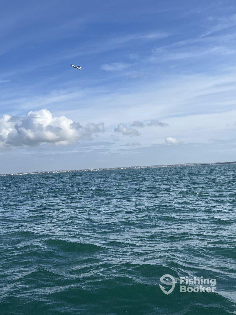 A scenic view of the ocean with a distant shoreline and a plane flying overhead, capturing the tranquil atmosphere of a fishing trip.