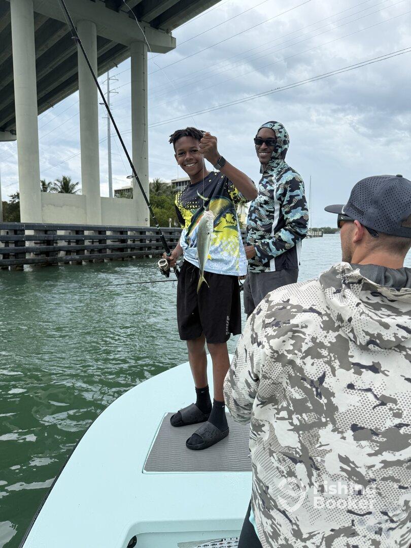 A young angler proudly displays a caught fish while fishing with friends under a bridge, showcasing a vibrant fishing environment.