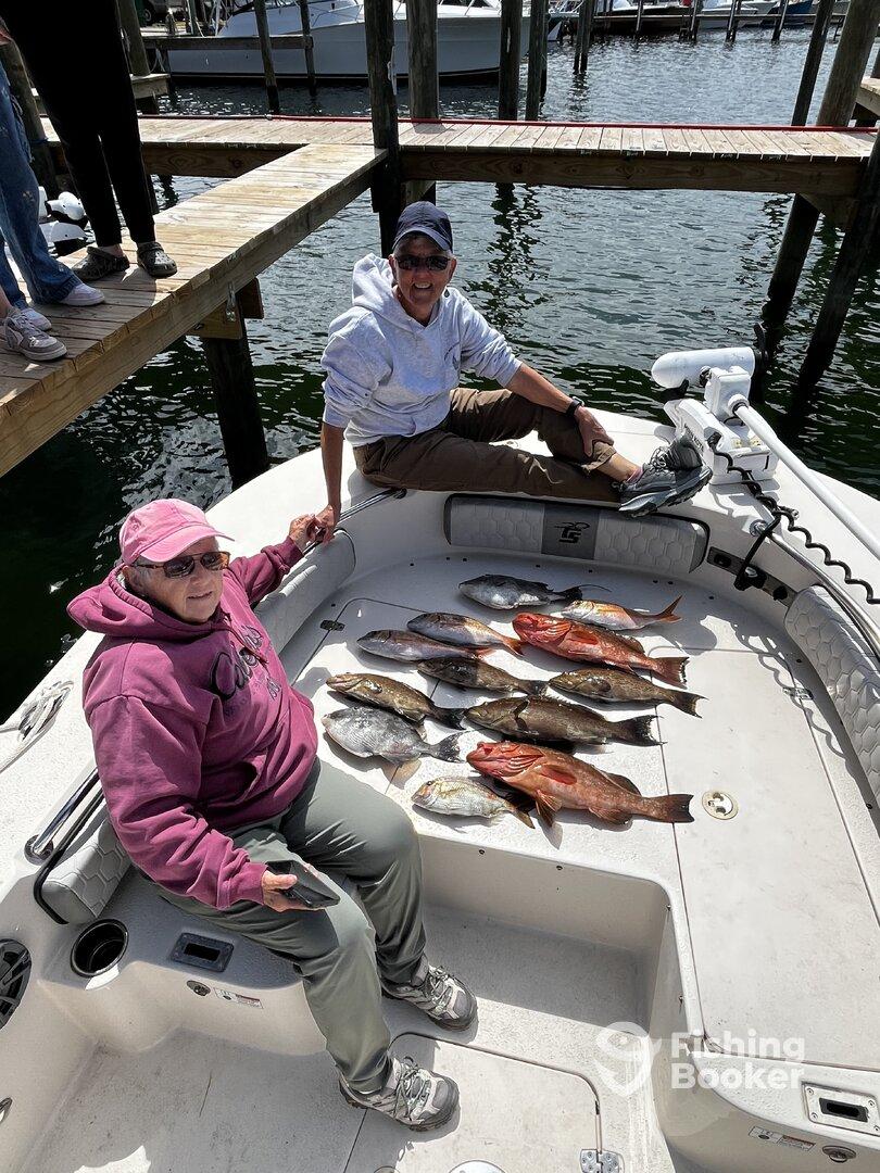Two anglers relaxing on the boat with a variety of freshly caught fish, including Snapper and Grouper, displayed on the deck after a successful fishing trip.