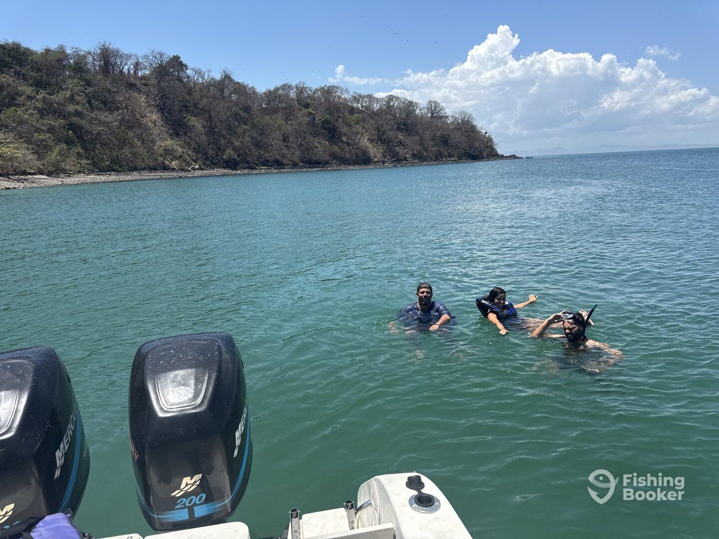 Three individuals enjoying a snorkeling experience in clear waters near a coastal area, with a boat partially visible in the foreground.