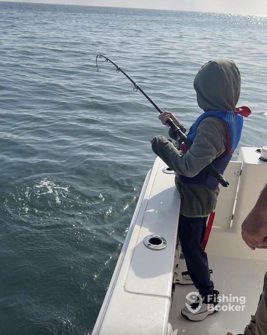 A young angler is actively reeling in a fish from a boat, showcasing the excitement of fishing in open waters.