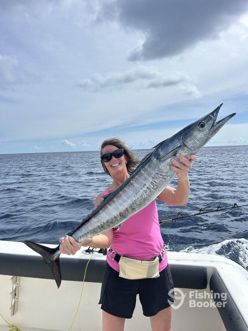 Angler proudly displaying a large Wahoo while fishing offshore, showcasing the excitement of a successful catch.