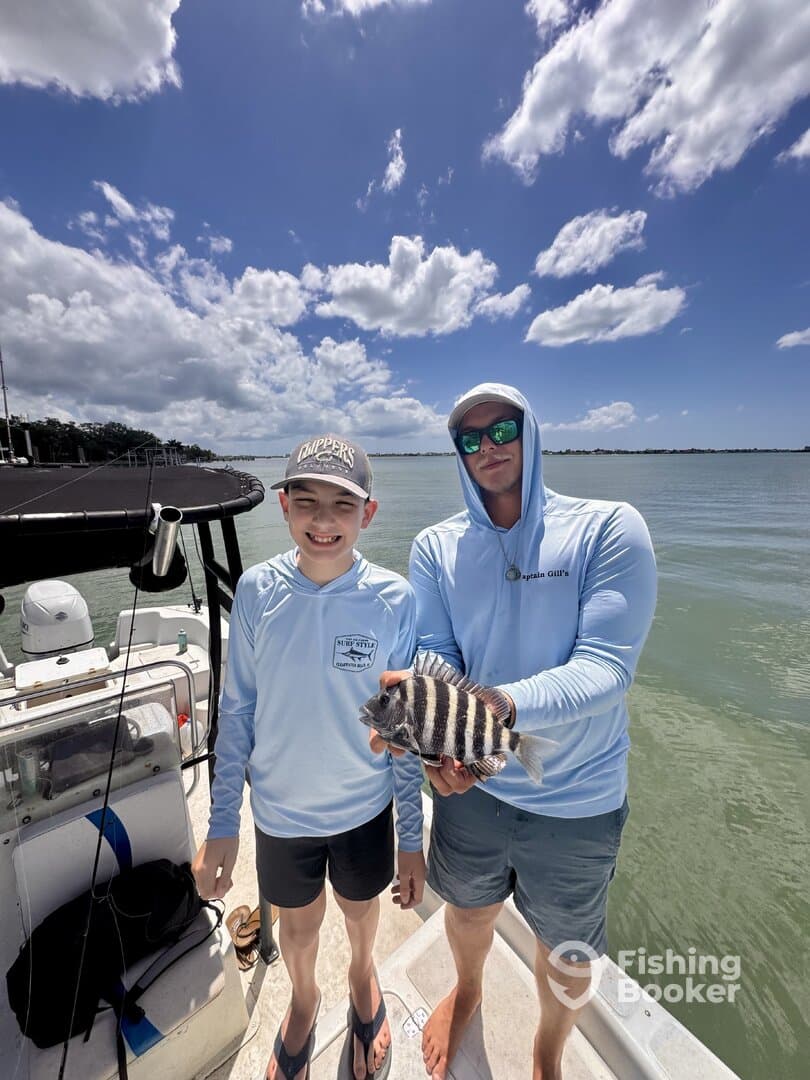 A young angler and an adult proudly display a striped fish on a boat, enjoying a sunny day on the water.