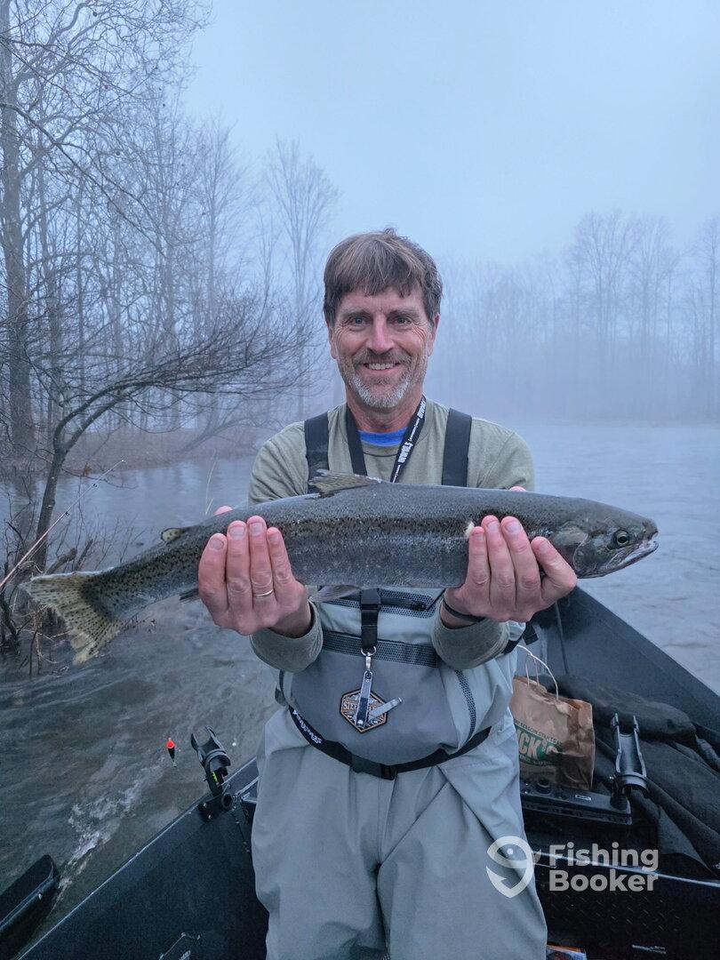 Angler proudly displaying a large Rainbow Trout while fishing in a foggy river setting.