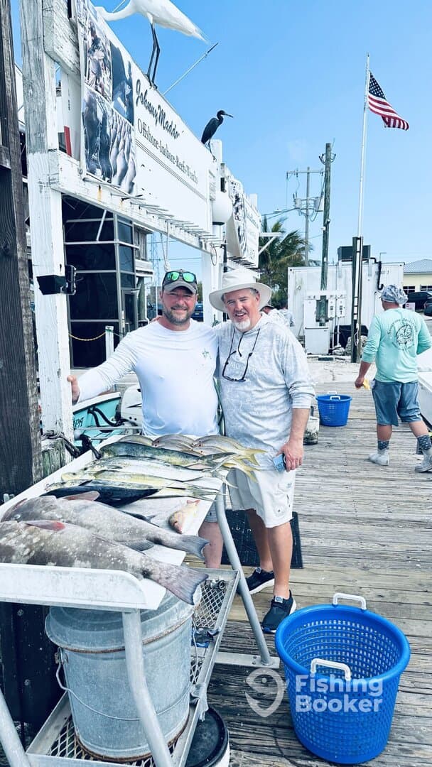 Two anglers proudly displaying their catch of various fish, including Mahi Mahi, at a dockside cleaning station after a successful fishing trip.