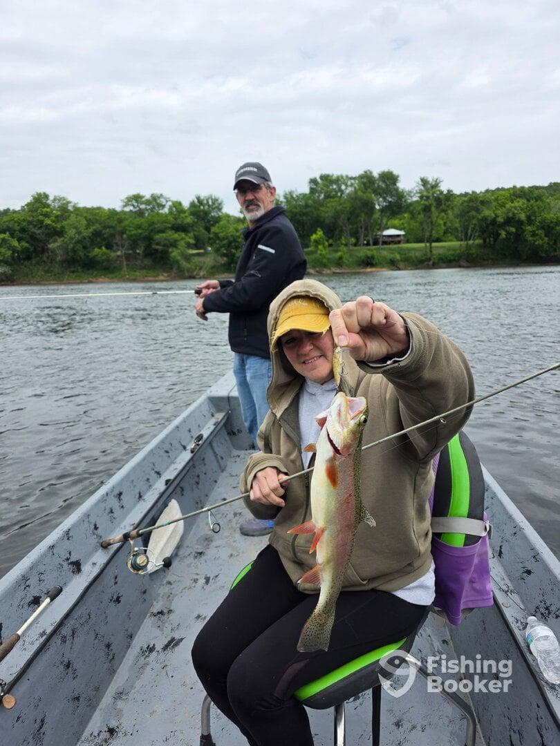 A young angler proudly displaying a freshly caught Largemouth Bass while fishing from a small boat on a calm river.
