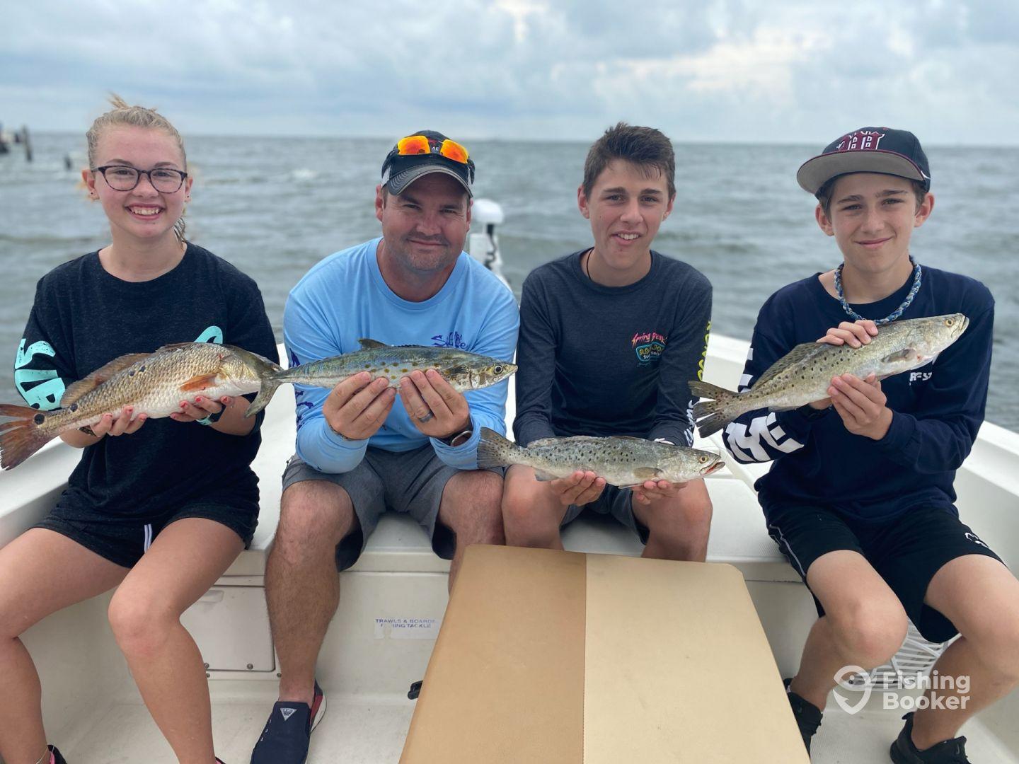 A group of young anglers proudly displaying their catches of Speckled Trout and Redfish while enjoying a day on the water.