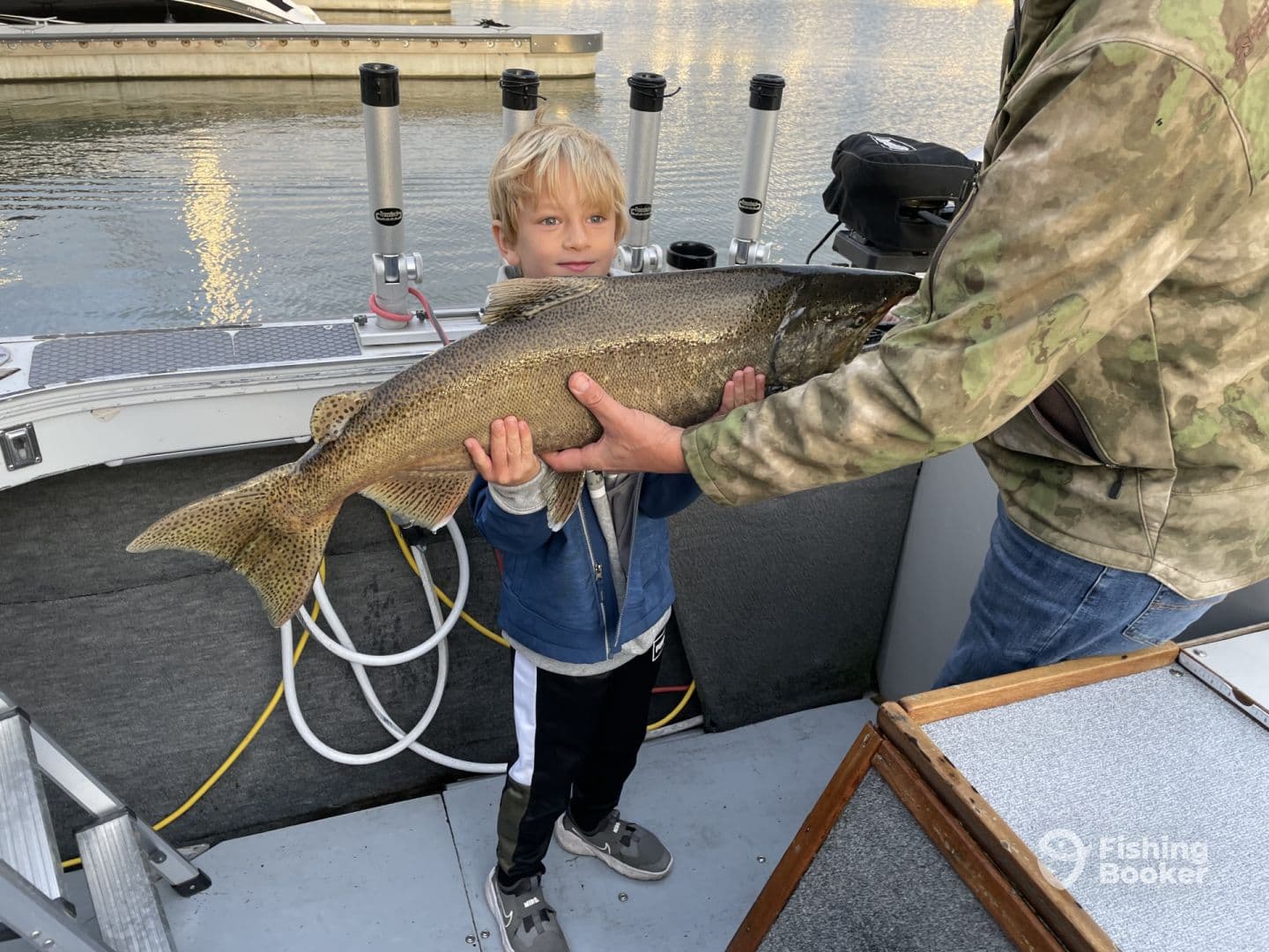 A young angler proudly displaying a large trout on a fishing boat, showcasing a successful catch during a family fishing trip.