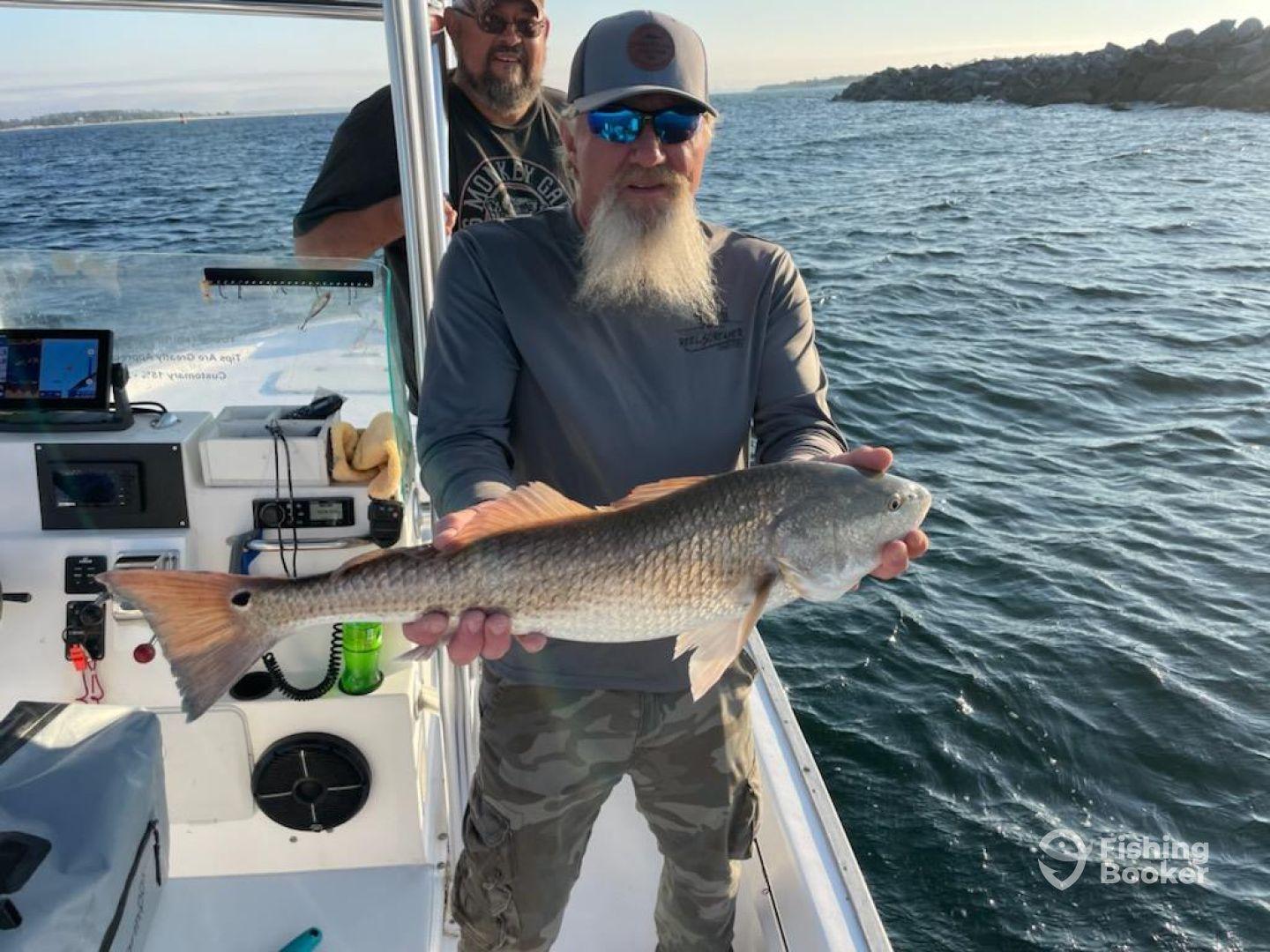 An angler proudly displaying a large Redfish while aboard a boat, with a scenic water backdrop.