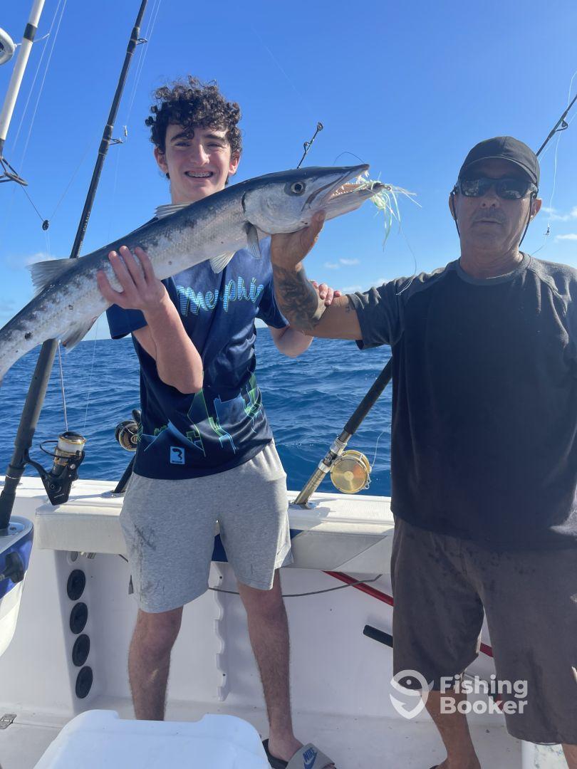 A young angler proudly displaying a large Barracuda while fishing on a charter boat in open waters.
