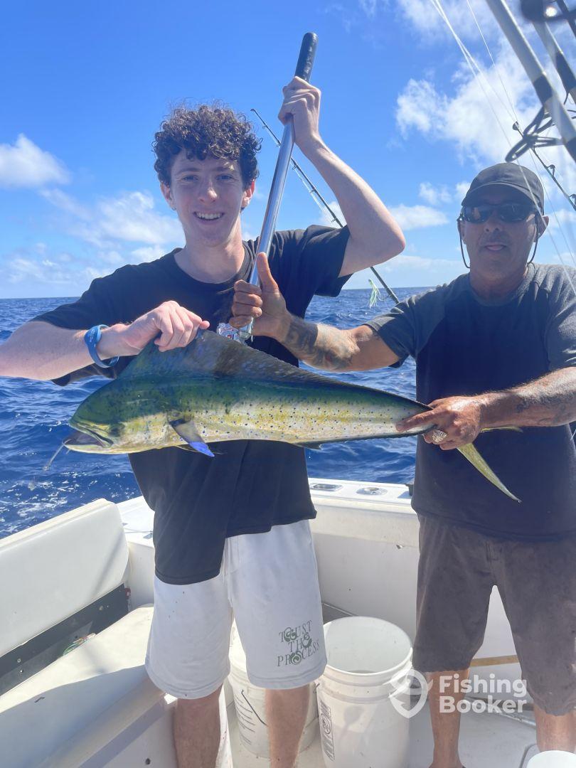 A young angler and a guide proudly displaying a vibrant Mahi Mahi aboard a fishing boat in open waters.