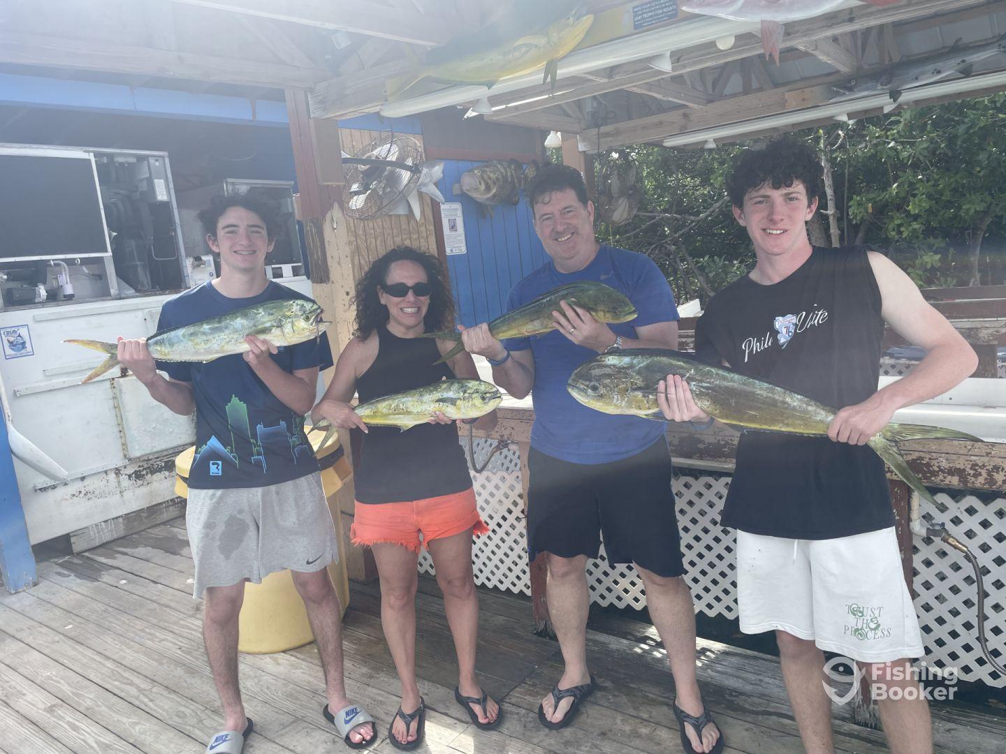 A group of four anglers proudly displaying their catch of Mahi Mahi at a fishing dock, showcasing a successful day on the water.