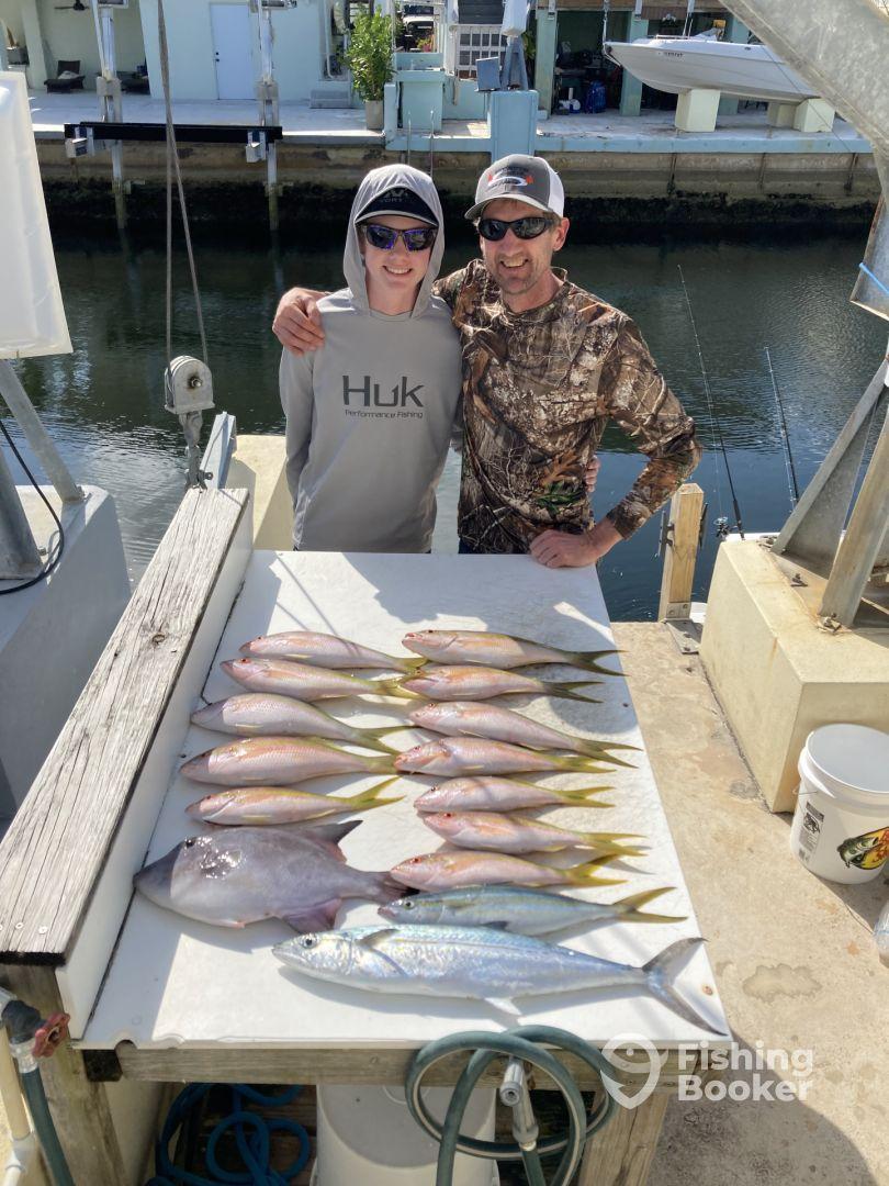 A young angler and an adult proudly pose with a variety of fish, including Snapper and Mackerel, displayed on a cleaning table after a successful fishing trip.