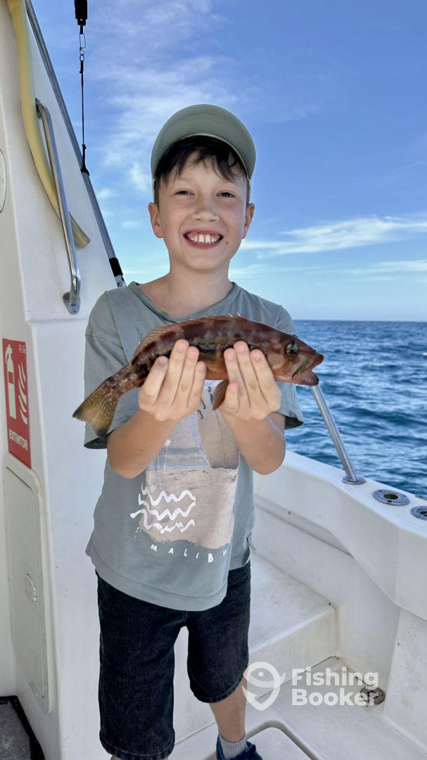 A young angler proudly displaying a colorful fish while aboard a fishing boat, enjoying a day on the water.