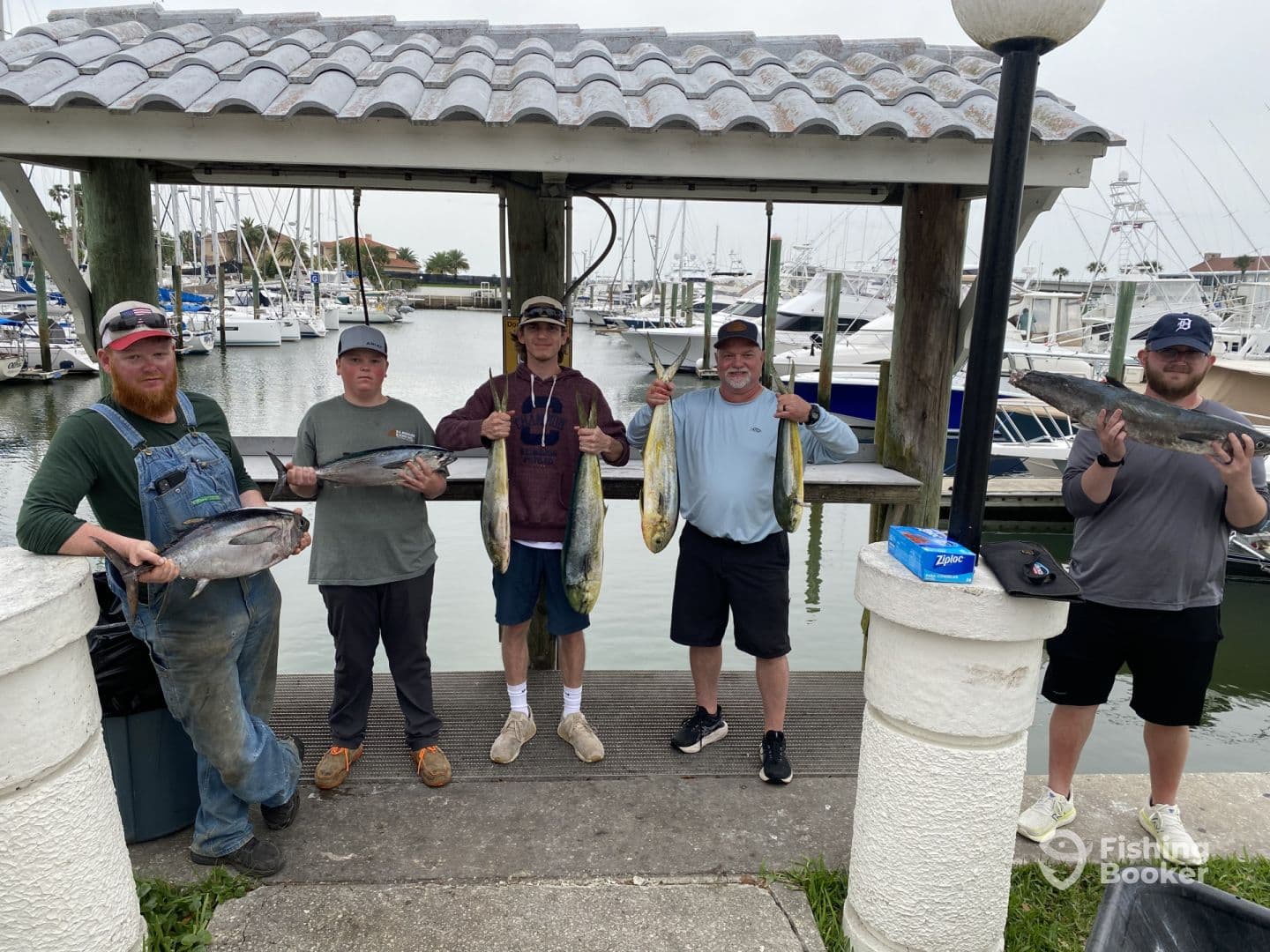 A group of anglers proudly displaying their catch, including Mahi Mahi and Tuna, at a marina after a successful fishing trip.