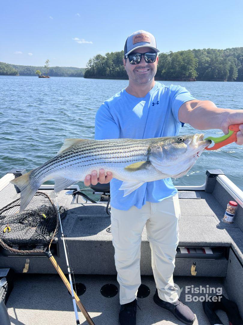 An angler proudly displaying a large striped bass while fishing on a serene lake, showcasing a successful day on the water.