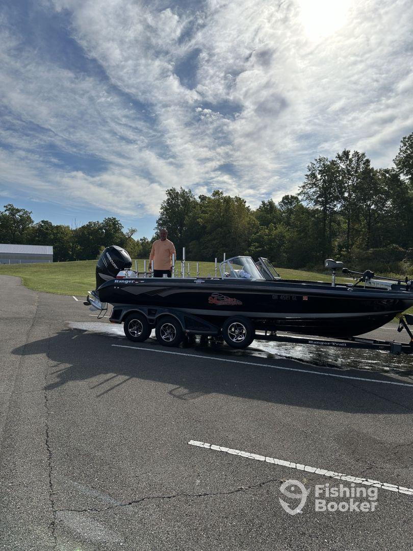 A man stands beside a sleek black Ranger boat, showcasing its exterior in a scenic outdoor setting.