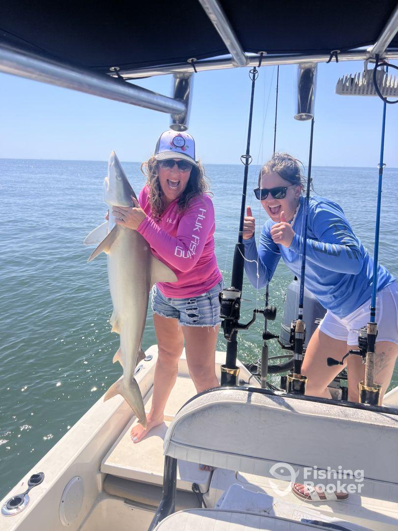Two excited anglers on a boat proudly displaying a large shark caught during a sunny day fishing trip.