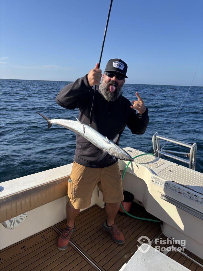 Angler displaying a large Barracuda while fishing on a boat in open waters.