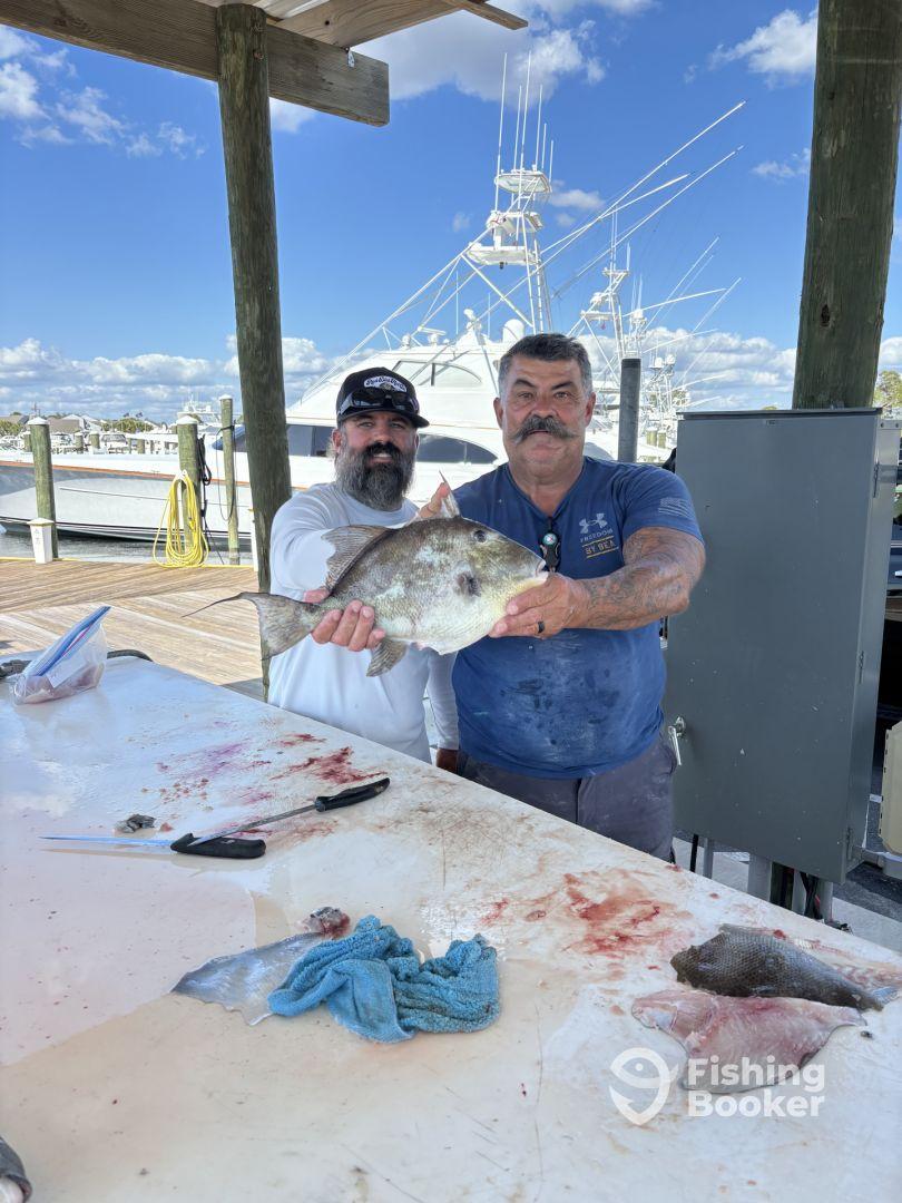Two anglers proudly displaying a large Snapper at the cleaning station after a successful fishing trip.