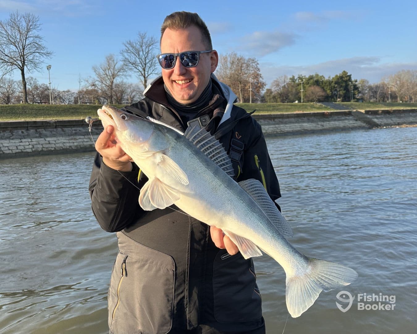 Angler proudly displaying a large Zander caught during a fishing trip, with a scenic riverside backdrop.