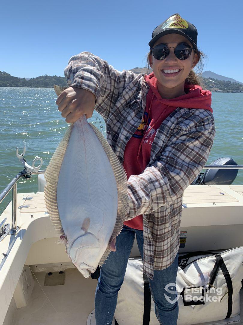 A happy angler proudly displaying a large Halibut while fishing on a sunny day in a scenic lake environment.