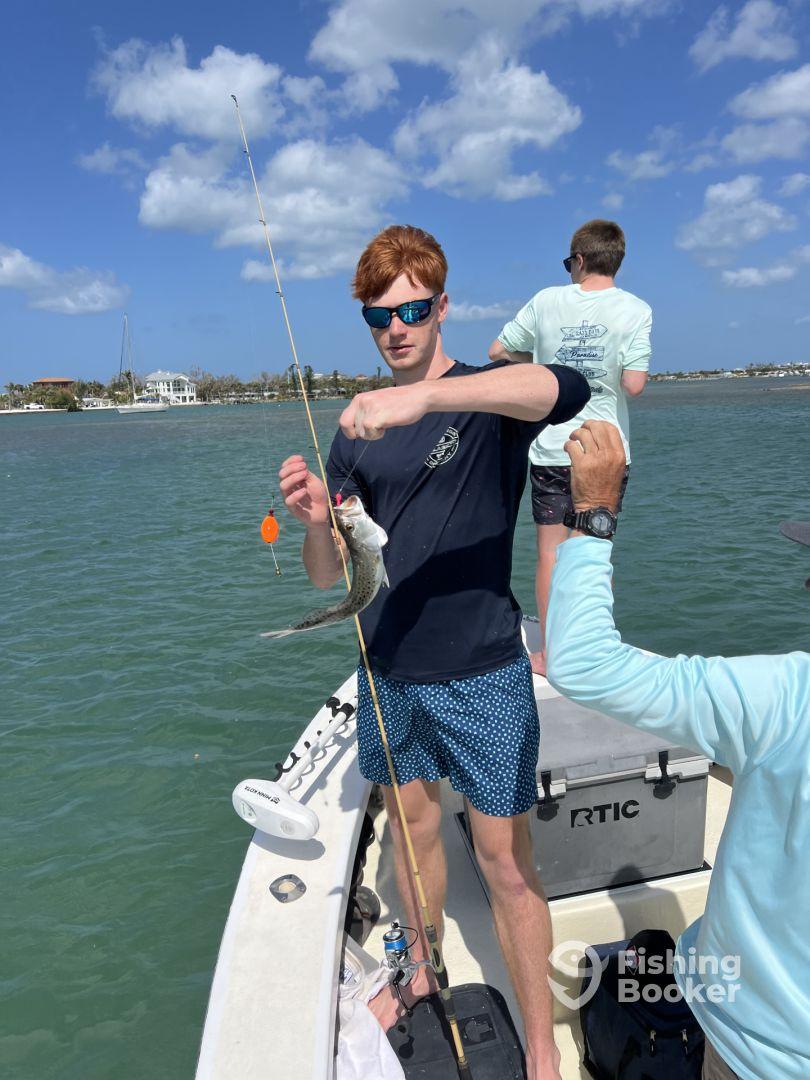 A young angler reeling in a fish while fishing on a boat in a sunny coastal environment, showcasing an engaging fishing experience.
