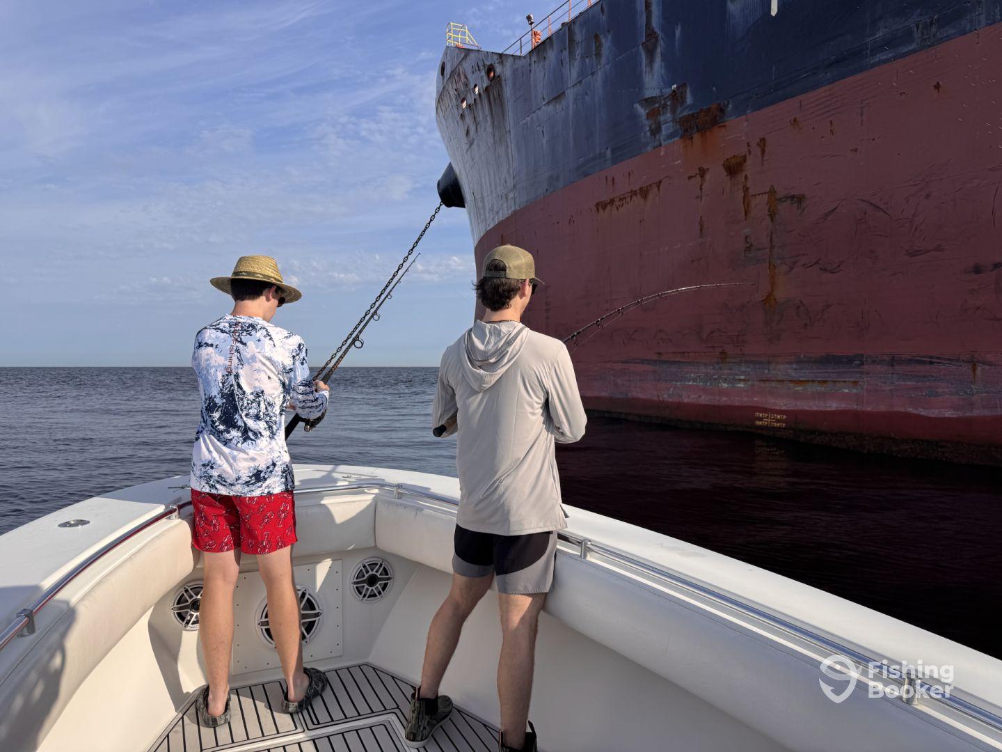 Two anglers actively fishing near a large ship in open water, showcasing the excitement of deep-sea fishing.